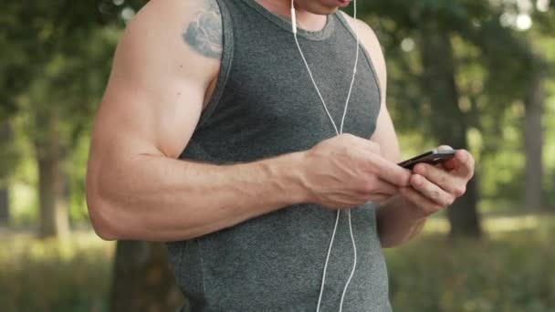 Jovem escolhe música no smartphone antes de correr — Vídeo de Stock