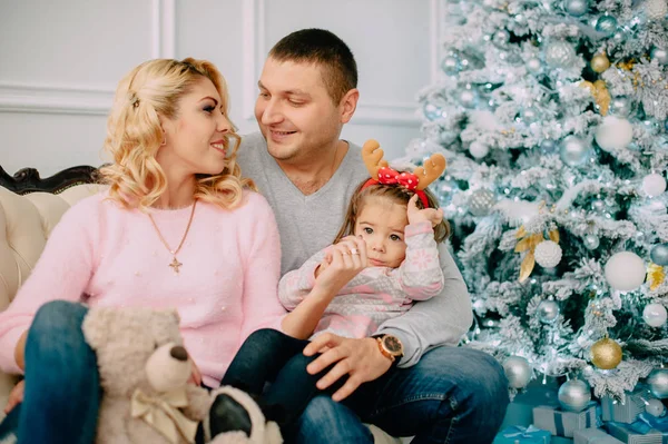 Junge Familie sitzt auf Sofa neben Weihnachtsbaum — Stockfoto