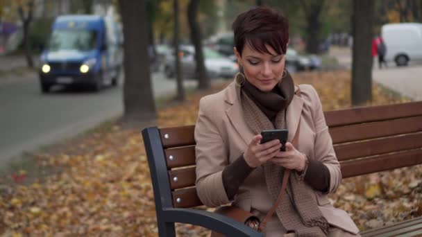 Giovane femmina utilizza smartphone mentre seduto sulla panchina — Video Stock