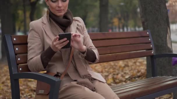 Junge Frau benutzt Smartphone, während sie auf Bank in der Stadt sitzt — Stockvideo