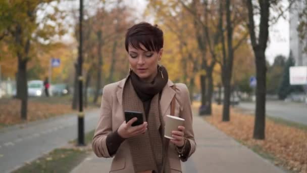 Giovane donna a piedi lungo la strada e utilizzando smartphone — Video Stock