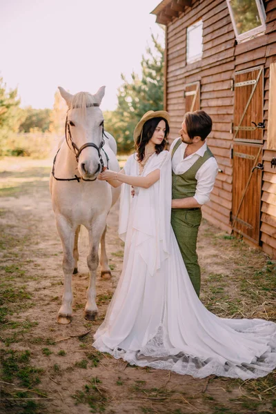 Élégants jeunes mariés câlins près du cheval, style champêtre — Photo