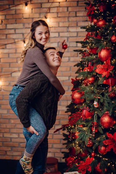 Pareja joven vistiendo árbol de Navidad en casa —  Fotos de Stock