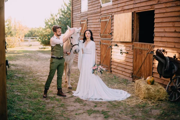 Sposi in stile boho in piedi vicino a cavallo in ranch — Foto Stock
