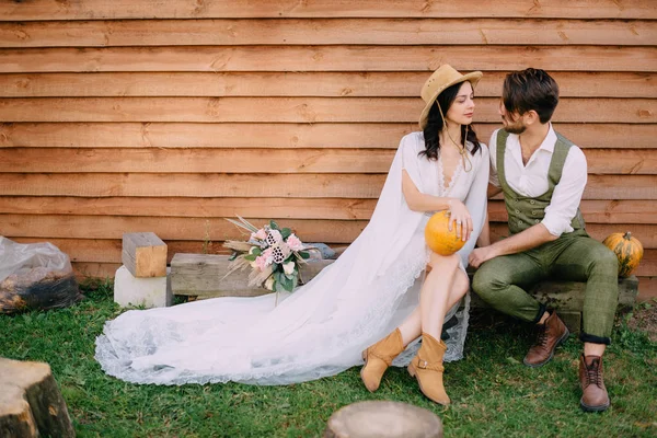 Nygifta klädd i boho stil sitta nära trävägg — Stockfoto