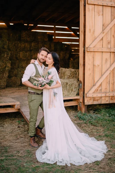 groom holds bride by hand while standing on ranch on sunny day