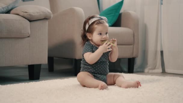 Baby girl nibbles toy while sitting on floor at home — Stock Video