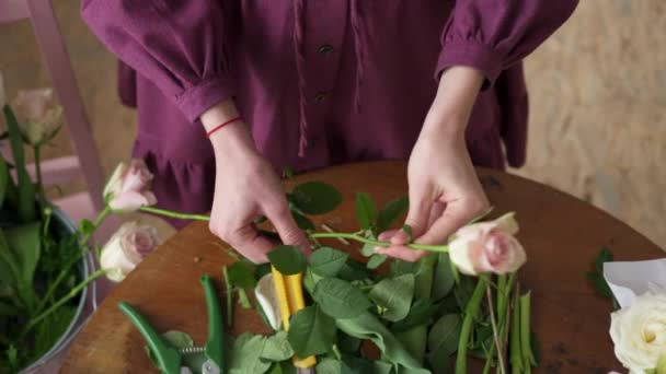 Fleuriste femelle nettoie les feuilles de tiges de rose, vue de dessus — Video