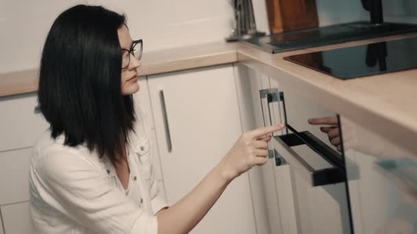 Mulher jovem ajusta a temperatura do forno na cozinha — Vídeo de Stock