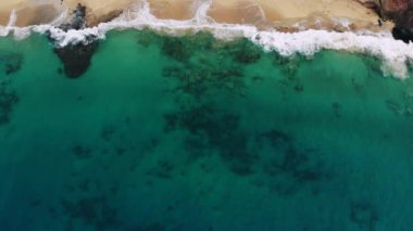 Hava manzaralı dalgalar beyaz kumsalda kırılıyor.