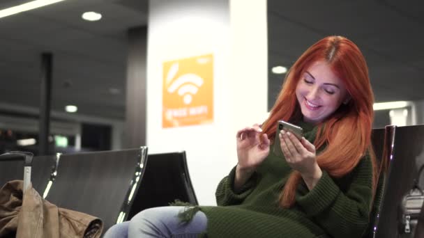 Joven feliz hembra utiliza el teléfono en la terminal del aeropuerto — Vídeos de Stock