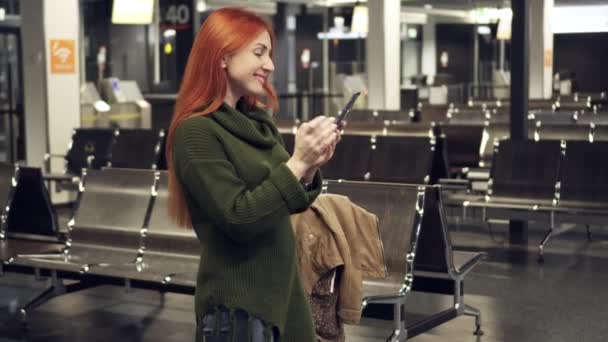 Joven hembra utiliza smartphone en terminal del aeropuerto nocturno — Vídeo de stock