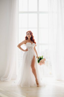 Kızıl saçlı gelin beyaz gelinlikle büyük pencere standları