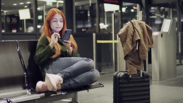 Joven mujer utiliza el teléfono en la terminal del aeropuerto — Vídeos de Stock