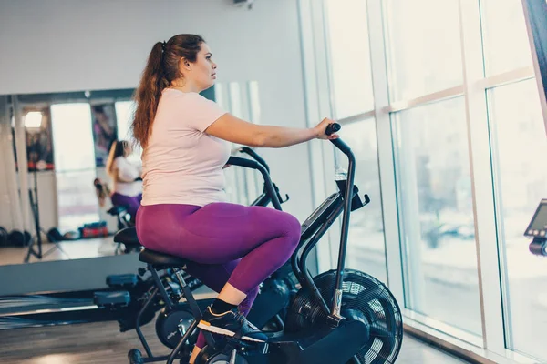 固定自転車で激しく運動する太った女性 — ストック写真