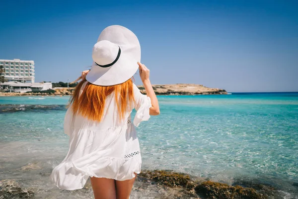 Руда жінка в Білій сукні стоїть зі спиною до камери на березі Середземного моря — стокове фото
