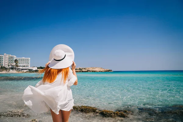 Щаслива жінка в білому одязі, стоячи на пляжі з кришталево чистою водою — стокове фото