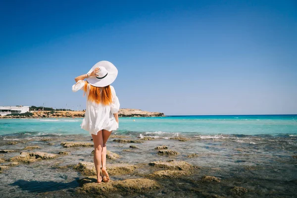Руда жінка в Білій сукні стоїть зі спиною до камери на березі Середземного моря — стокове фото