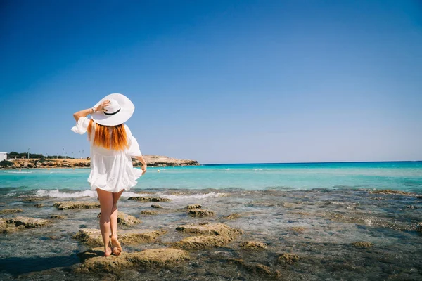 Жінка туристична біла сукня, що стоїть на пляжі з кришталево чистою водою . — стокове фото