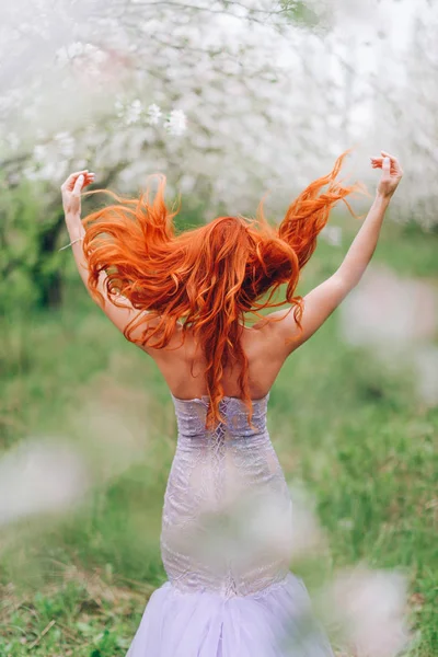 Рыжая женщина бросает волосы в цветущий весенний сад — стоковое фото