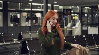 Havaalanı terminalinde yürüyen ve telefonla konuşan genç bir kadın.