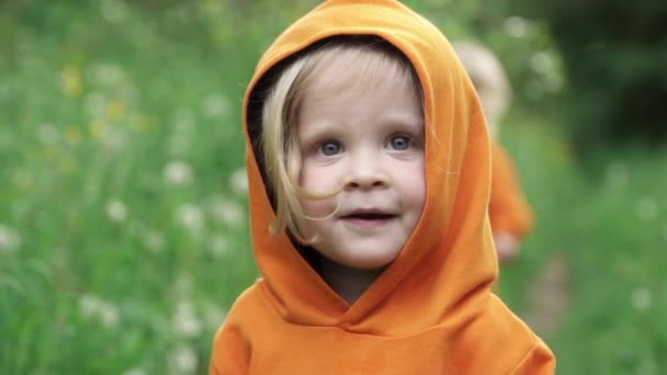 Liten pojke i ljust orange hoodie ser in i kameran och ler — Stockvideo