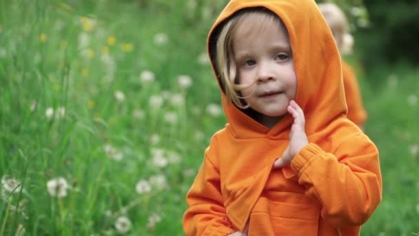 Kleine jongen in fel oranje hoodie kijkt in de camera en glimlacht — Stockvideo