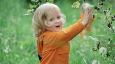 turuncu kapüşonlu küçük neşeli çocuk doğada yürüyüş sırasında kameraya bakar, yavaş hareket