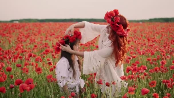 Joven madre pone corona de flores de amapola en la cabeza de sus hijas, cámara lenta — Vídeos de Stock