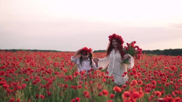 Mãe feliz e filha estão correndo através do campo de papoula florescendo ao pôr do sol, câmera lenta — Vídeo de Stock