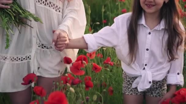 Close-up mãe e filha ir de mãos dadas no campo de papoula florescendo ao pôr do sol, câmera lenta — Vídeo de Stock