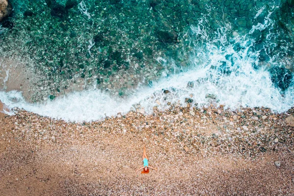 Вид з повітря на молоду жінку, що лежить на гальковому пляжі біля морських хвиль — стокове фото