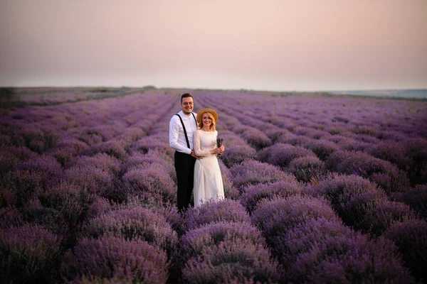 Heureux jeunes mariés se tiennent dans le champ de lavande en fleurs au coucher du soleil — Photo