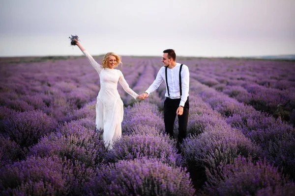 Joyeux jeunes mariés courant le long du champ de lavande en fleurs — Photo