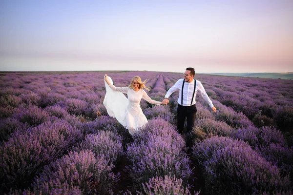 Joyeux jeunes mariés courant le long du champ de lavande en fleurs — Photo