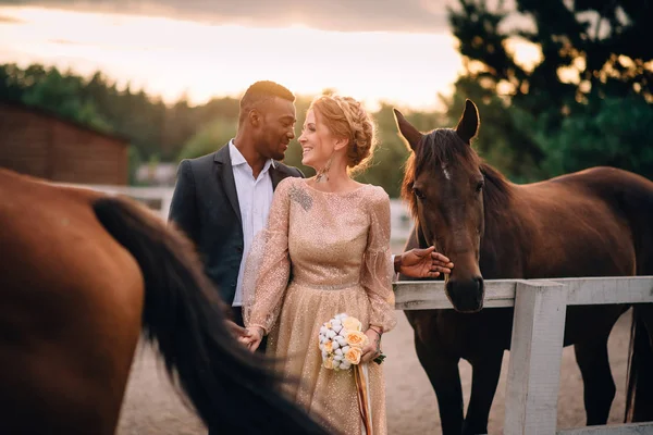 Heureux jeunes mariés souriants debout sur le ranch entouré de chevaux . — Photo