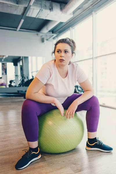 Obese woman sits on gym ball in gym