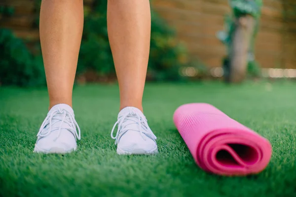 Közeli női lábak állni a zöld fű közelében fitness mat — Stock Fotó