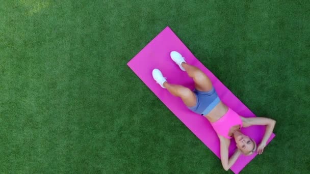 Vue du dessus jeune femme athlétique entraîne les muscles abdominaux tout en étant couché sur l'herbe — Video