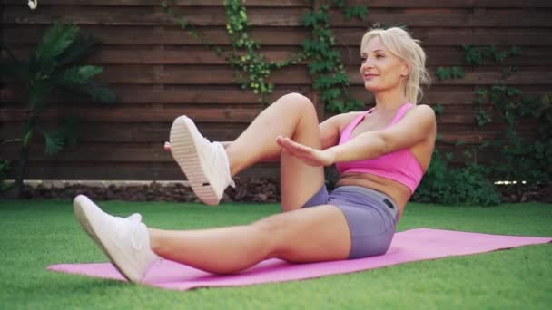Mulher atlética jovem treina músculos abdominais deitado na grama verde — Vídeo de Stock