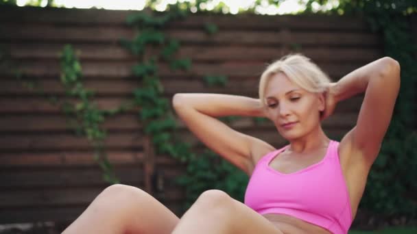 Mujer atlética joven entrena los músculos abdominales que yacen en la hierba verde, cámara lenta — Vídeo de stock