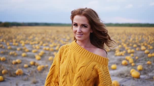 Joven mujer sonriente sosteniendo la calabaza en sus manos y mirando a la cámara mientras está de pie en el campo — Vídeos de Stock