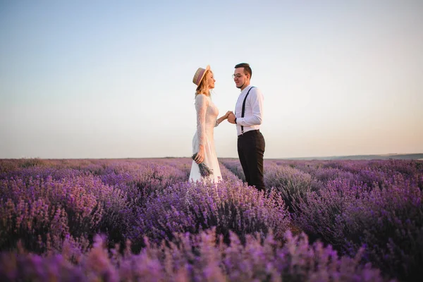 Šťastní novomanželé stojí v kvetoucím levandulovém poli při západu slunce — Stock fotografie