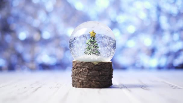 Close-up de flocos de neve girando em torno de uma árvore de Natal dentro de uma bola de vidro — Vídeo de Stock