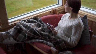 Rahat sandalyedeki kadın yağmurlu bir günde akıllı telefon kullanıyor.