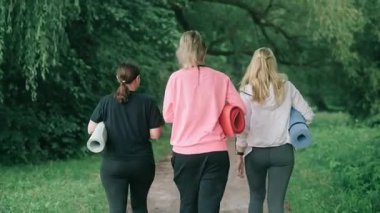 Üç orta yaşlı kadın spor yapmak için parka gider. Arka görünüm.