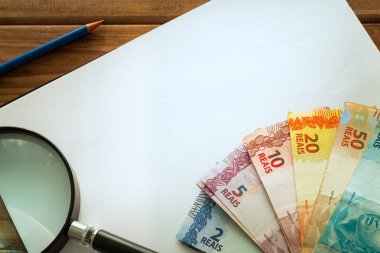 Brezilya para, Reali, beyaz boş bir kart, bir büyüteç ve bir kalem ile masada