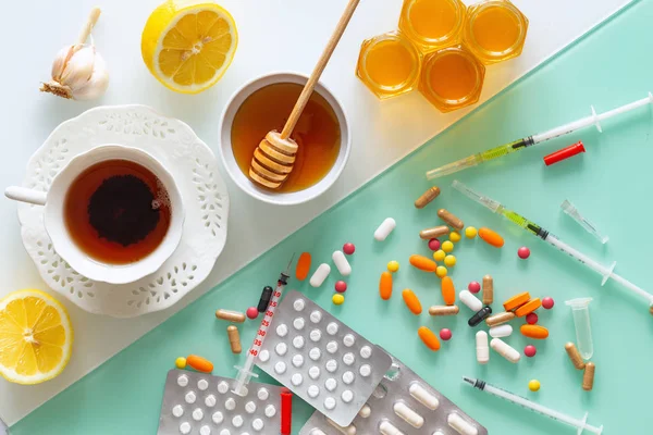 natural medicine, tea, honey, lemon and garlic against tablets of syringes and other medications, top view background in two colors, white and green pastel