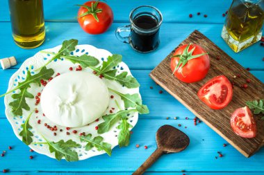 Burrata, domates, baharat, argugula ve zeytinyağı ve balsamik sirke/mavi ahşap masa ile Italyan peyniri