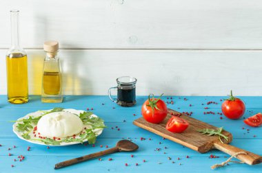 Burrata, domates, baharat, argugula ve zeytinyağı ve balsamik sirke / mavi ahşap masa / metin için yer ile İtalyan peyniri